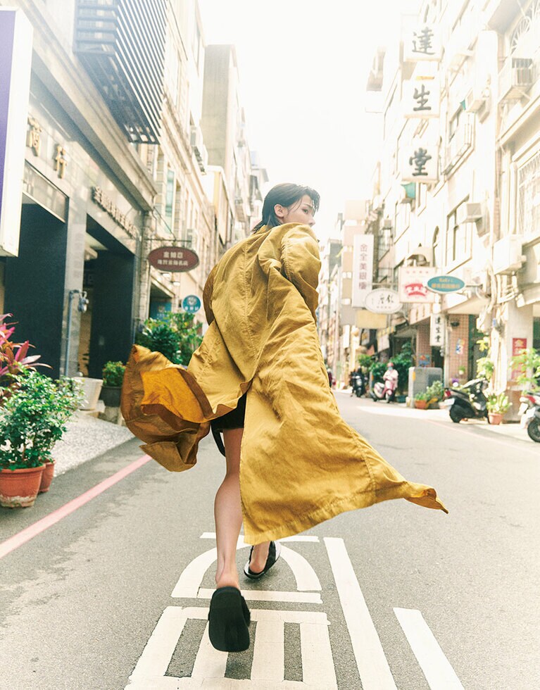 【新竹】東前街（ドンチェンジェ）“台湾のシリコンバレー”と呼ばれる一方で、旧市街地には風情ある街並みが残るのも新竹の魅力。東門市場を背に、東前街を駆け抜けて。近くには1930年代の百貨店をリノベした話題のカルチャースポット「或者新州屋」も。コート、ショートパンツ、サンダル／ドリス ヴァン ノッテン