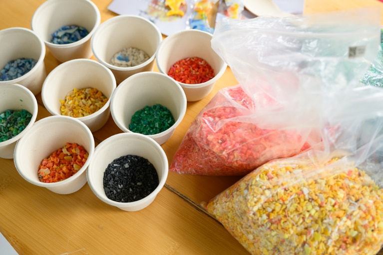 海洋プラスチックを粉砕して作ったカラフルなチップ。着色は一切なしで、色は元のプラスチックそのまま。知床（オレンジ色）、奄美大島（赤色／緑色）、奥尻島（黄色）など、拾われた地域別になっていた。