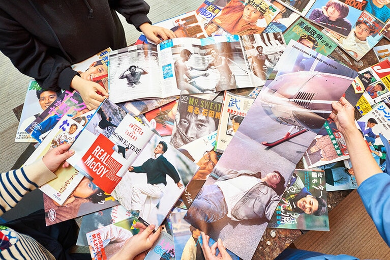 ヘリコプターの元に寝転ぶ風間トオルなどお宝ショットの観音開きのページ。『風間トオル’91CITY』『僕らのセーターアイランド 風間トオルと仲間たち』(ともに雄鶏社)より。