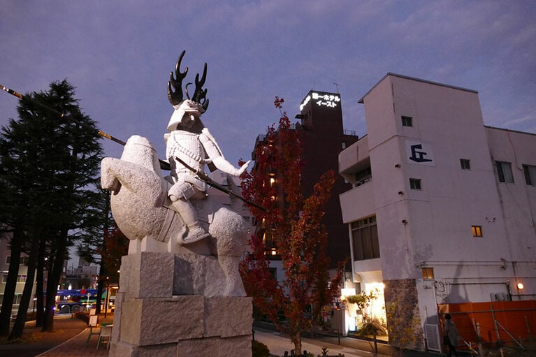 「ちょっと待て？」左手のポーズが謎の武将の後ろに「丘」と描かれたビルが。