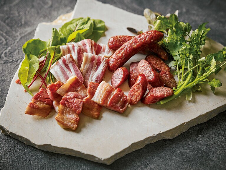 火山研究家でもある青木章さんがチップを使わず、桜とナラの薪で燻し上げるベーコンとソーセージ。塩、胡椒のみで味つけし、赤レンガの燻製窯で約8時間かけてスモーク。スモークハウス白南風の燻製 2種 3,456円(税込)。