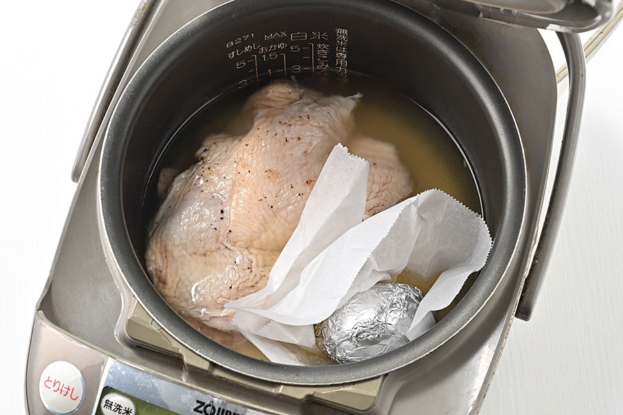 鶏肉の脇にクッキングシートを袋状に立ち上がりを付けて置き、アルミ箔で包んだ卵のせる。