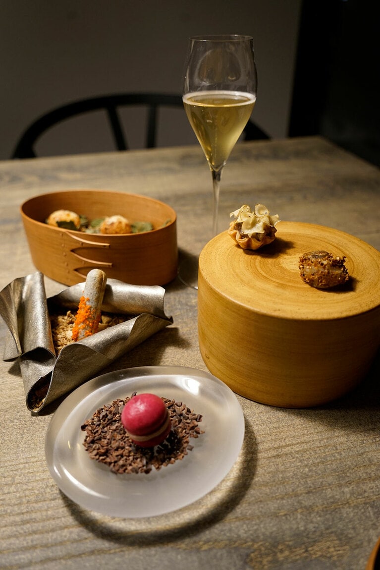 5種類の美しいアミューズ。手前から時計回りに、L'évo鶏レバーペーストを挟んだビーツのマカロン、香箱ガニが入った細長い八尾もなか、ヤギのチーズのグジェール、熊の手のタルト菊芋チップ載せ、山椒の殻をまぶした深海魚のゲンゲ。