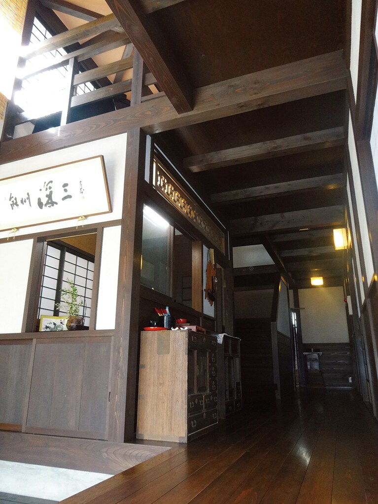 【民宿 深三】吹き抜けの開放的な玄関。建物に使われている木材のほとんどが能登ヒバや杉など地元産。宿主がまめにメンテナンスをしているため、味わいのある木の風合いに。2階には輪島塗や地元作家のアートワークスが並ぶギャラリースペースがある。
