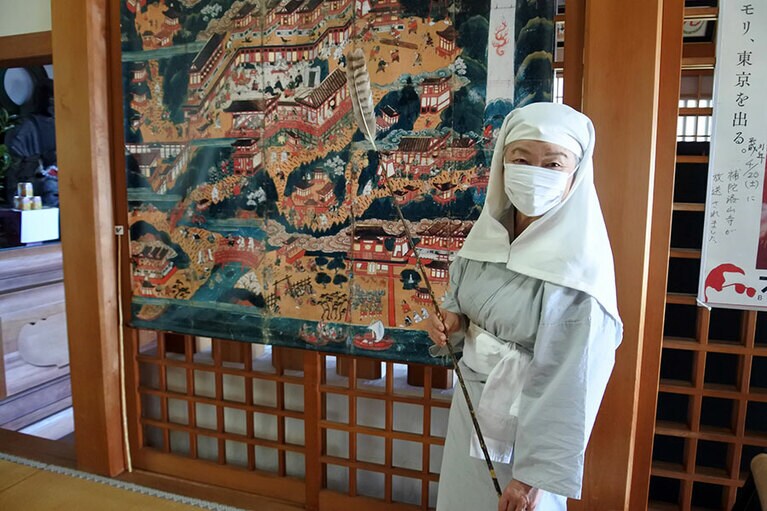 16世紀に平安時代の熊野信仰を描いた曼荼羅絵。各地で熊野信仰の布教につとめた比丘尼(びくに)の衣装を身に着けたガイドの山本妙子さんが曼荼羅図を絵解き。下の方に補陀落渡海の様子も。