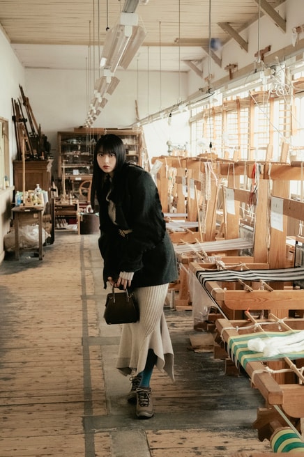 建物内では秩父銘仙の歴史や展示品を見ることができるほか、型染めや織りの体験も可能。木製の織り機や設備はすべて現役で使われているので、職人が織りを行う姿に出会えることも。菊池さん着用：ターギー フォー ウォータープルーフ ¥24,200／キーン（キーン・ジャパン）、ジャケット 96,800円、ベルト 36,300円／共にフミエタナカ（ドール）、ニットトップス 57,200円、ニットスカート 52,800円／共にオープン セサミ クラブ バッグ 37,400円／ルメメ、タイツ／スタイリスト私物