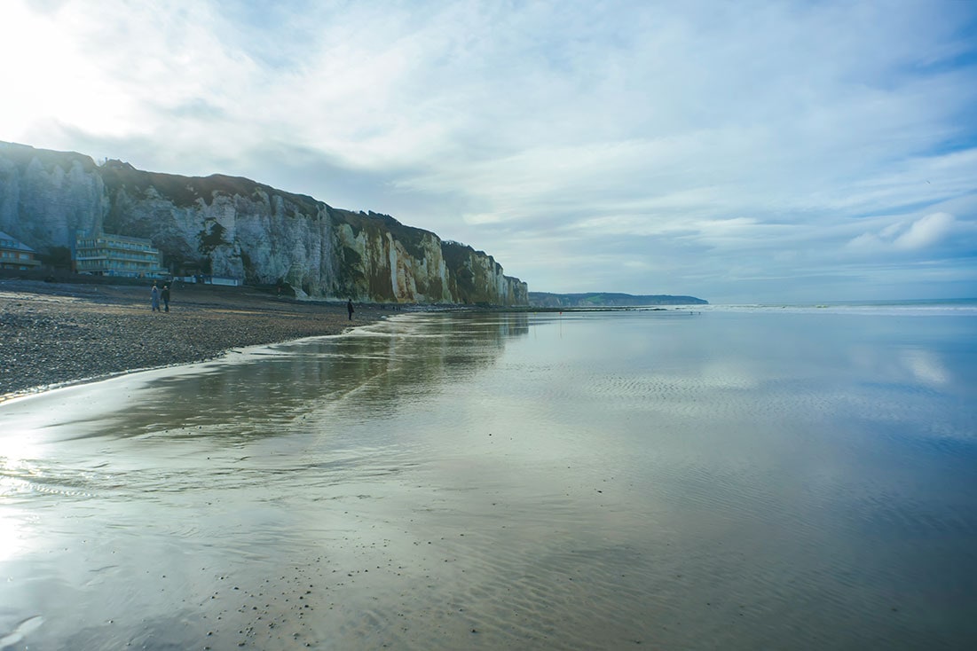 ベージュの砂浜が、青空そして断崖の影を映し込む。