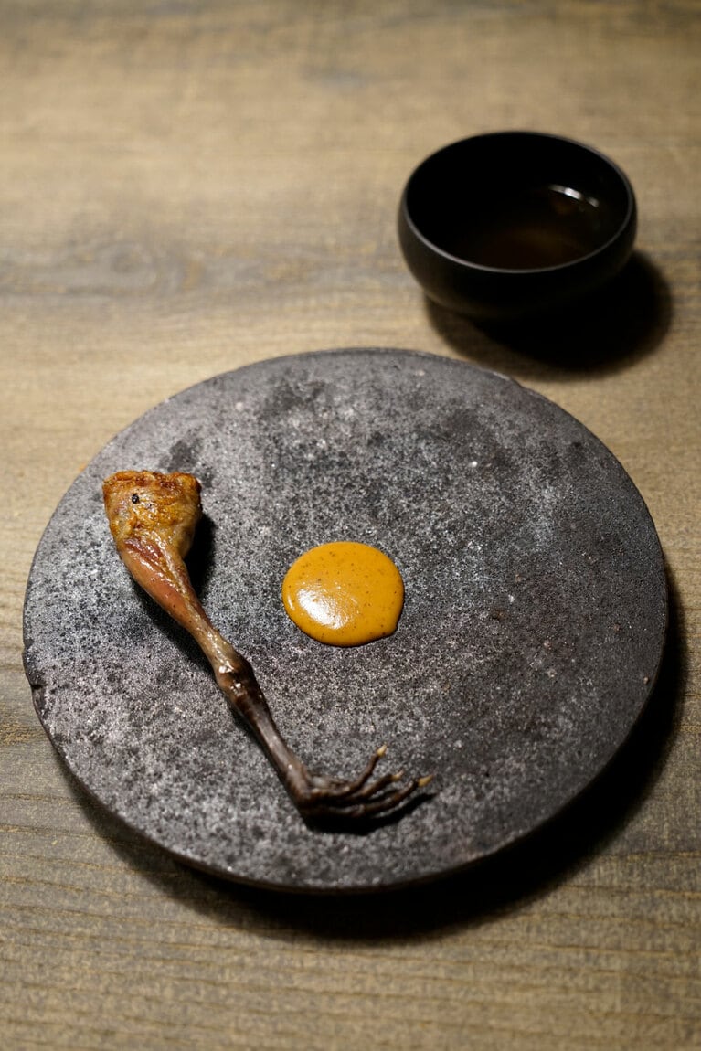 L'évo鶏。ベースとなる鶏は、満寿泉の酒粕などを飼料に使って、谷口シェフが生産者さんとともに開発したもの。中に熊の内蔵で炊いたご飯を詰めて焼いている。鶏と熊がお互いを引き立てている。器は、東岩瀬を拠点とする釋永岳さんが、「レヴォ」の敷地内の土を練り込んで焼きあげたオリジナルだ。