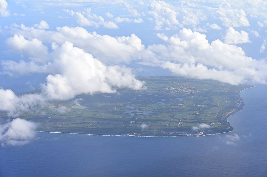 飛行機の窓から眺める南大東島。青い海のなかにポツンと緑の大地が浮かんでいます。