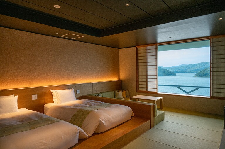 障子を開ければ穏やかな浜名湖の絶景が広がる客室。ベッドスローやクッションには、浜松の伝統的な織物、遠州綿紬が使われている。