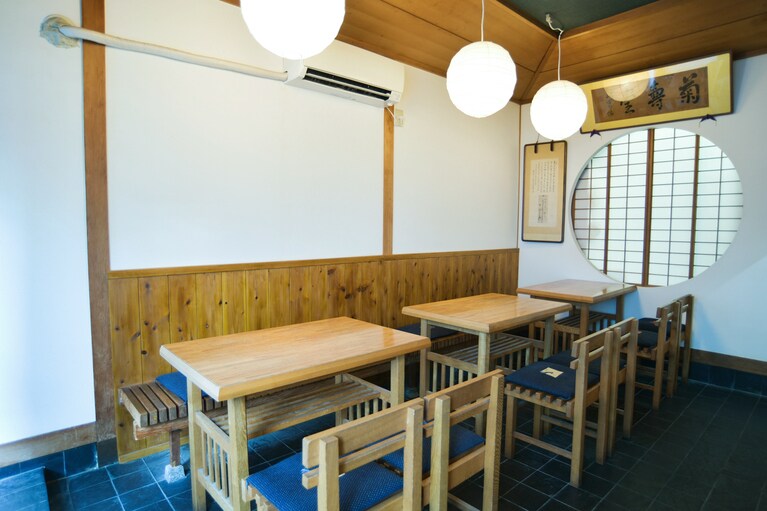 テーブルのみの店内。奥には、義太夫節の太夫で、人間国宝の山城少掾直筆の額が飾られている。