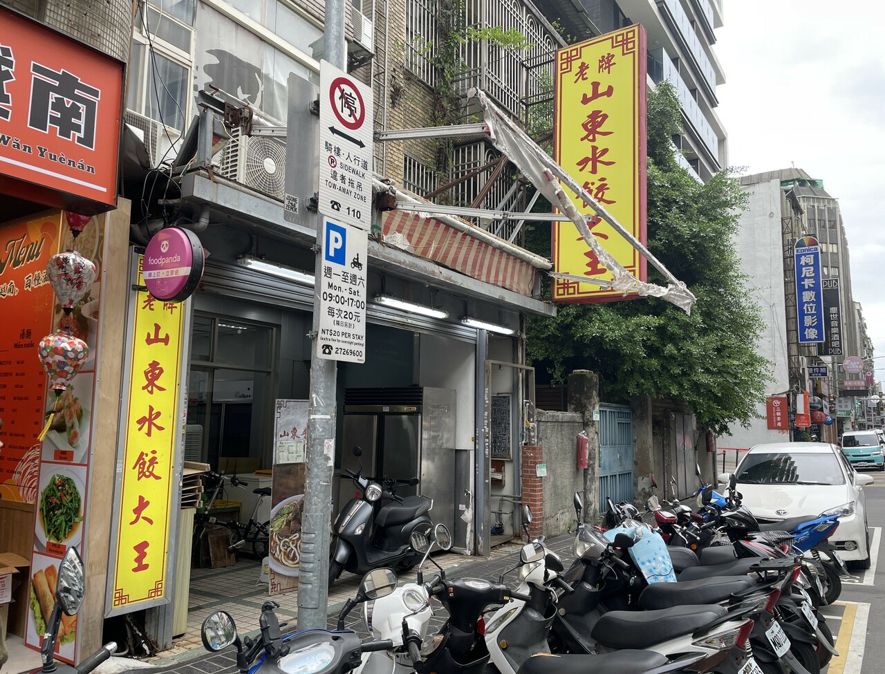 看板は通りの反対側からなら見つけやすいものの、同じ側を歩いていると木や屋根付き歩道に隠れて見逃してしまうことも。通り過ぎないようご注意を。