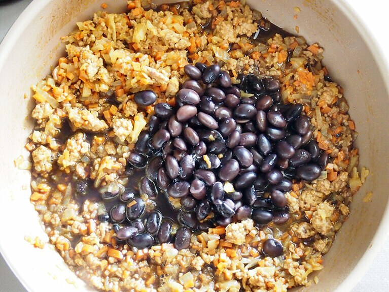 (7) 野菜が柔らかくなってきたら、［A］の調味料を入れて味付けをします。全体を混ぜたら、(3)の黒豆を煮汁ごと入れます。