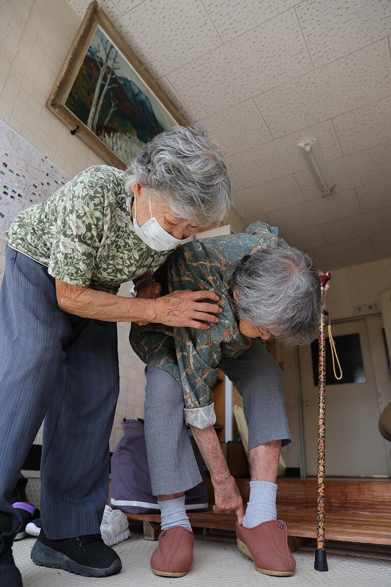 帰りに靴を履く哲代さん（右）を仲間が支える。
