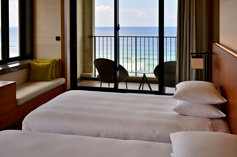 ベッドからも青く輝く海を眺められる人気の客室 “オーシャンコーナースイート”。