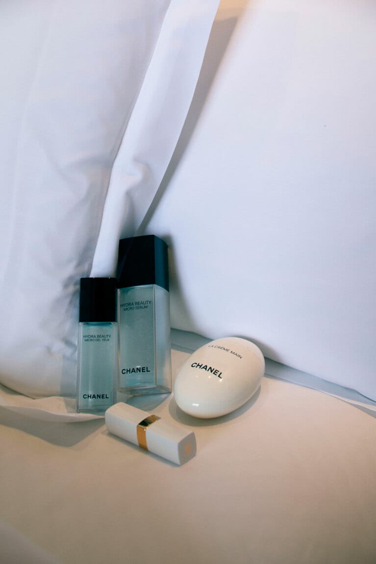 左から時計まわりに：「目もとのケアも欠かせません」シャネル イドゥラ ビューティ マイクロ アイ ジェル、「乾燥肌なので飛行機の中でも保湿を心がけています。セラムはさらっとした質感がすごく心地いい」同 イドゥラ ビューティ マイクロ セラム、「持ち運ぶのにいいサイズ感で、フォルムもかわいい。季節を問わずいつも携帯しています」同 ラ クレーム マン、「スティックタイプで塗りやすいです。機内は乾燥するのでこまめに塗っています」シャネル ルージュ ココ ボーム 912(すべて飯島さん私物)