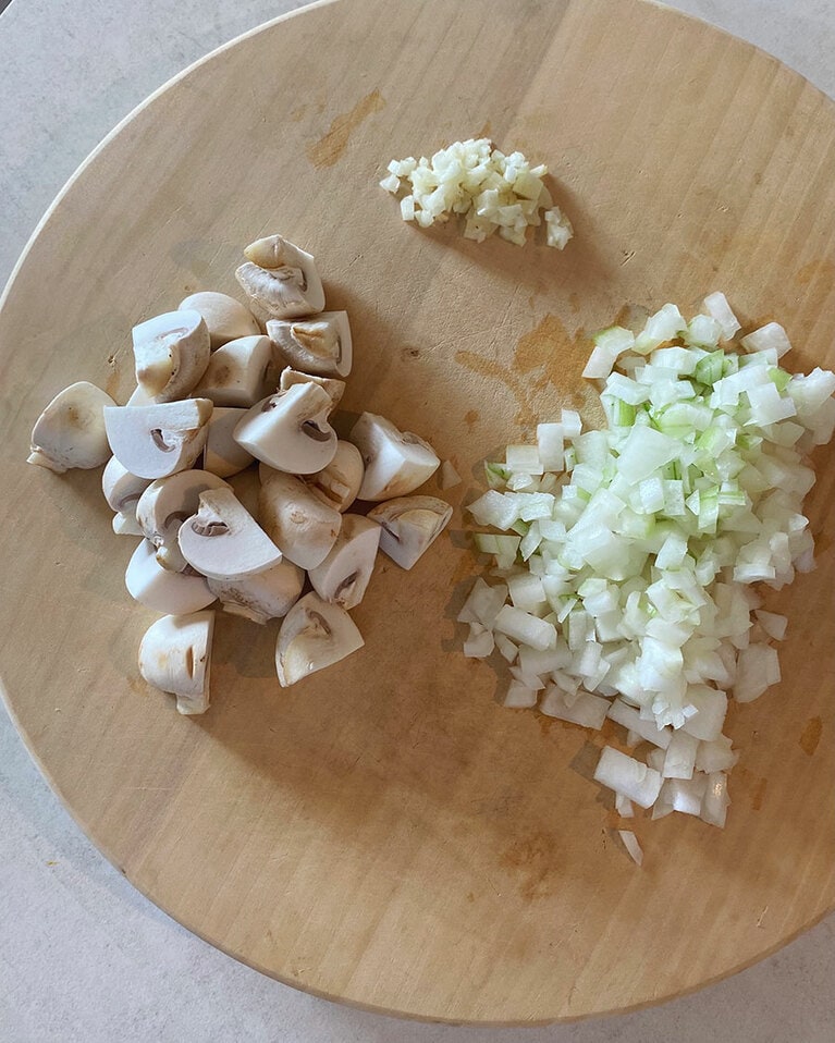 【ごろっと豚肉とマッシュルームのパセリバター炊き込みごはん】(1) マッシュルームは柔らかい布等でさっと汚れを拭い、軸の先端を切り落としたら軸を下にして縦十字に切る。玉ねぎとにんにくはみじん切りにする。