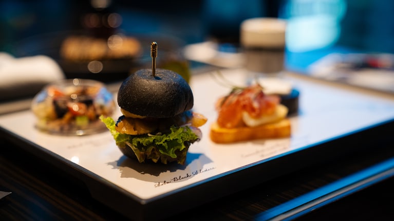 ブレインフーズとして、集中力の維持が期待できるカカオニブや、脳の活性化効果があるとされているサバを使用した「サバのブラックスライダー」（写真）などのメニューをラインアップ。また、ドレッシングの器にモンブランのインクボトルを使用するなど、ブランドの世界観を感じさせる遊び心ある演出も随所に。