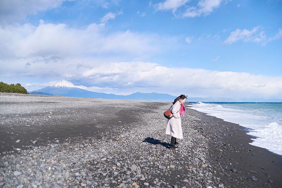 三保の松原で波打ち際を覗き込む永井さん。冬の青空に、雪を冠した富士山がくっきりと浮かび上がる。