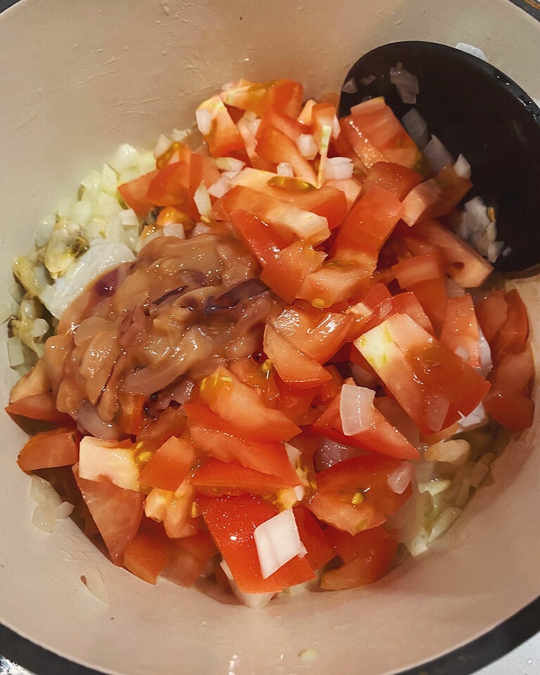 【ブイヤベースごはん】(4) トマトと塩辛を加えてざっと混ぜ合わせる。トマトから水分が出てきたら、白ワイン、おろしたにんにくを加えて蓋をして弱めの中火で8分加熱する。