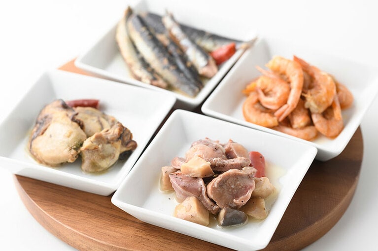 タパス各種。左から時計回りに：牡蠣のアヒージョ、いわしのオイルサーディン、小エビのアヒージョ、砂肝とエリンギのアヒージョ。