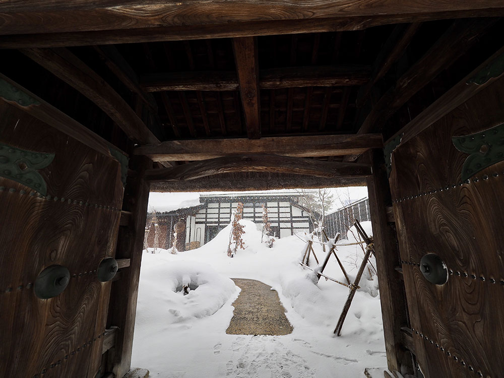 茅葺き屋根の薬医門をくぐり、母屋へ。冬の間はすっぽりと雪に包まれる。