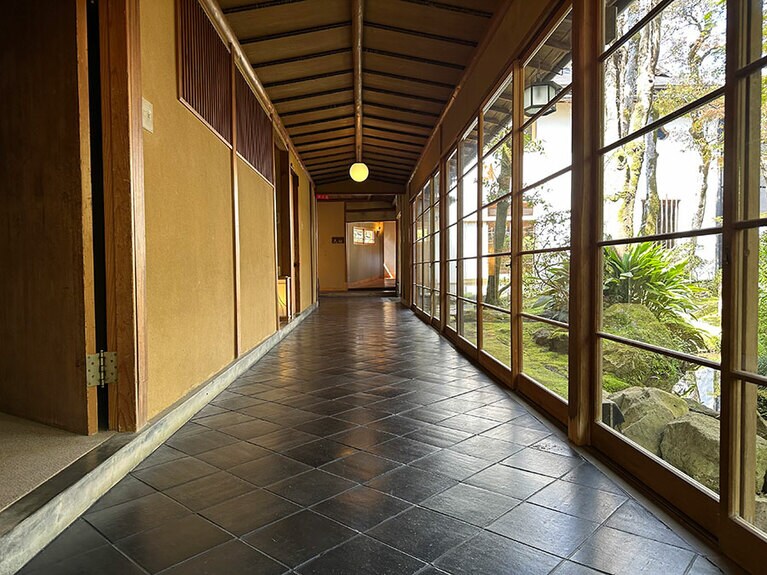 真っ黒な瓦が敷かれた廊下。ゆがみのある大正ガラス越しに古木を見ながら通る。
