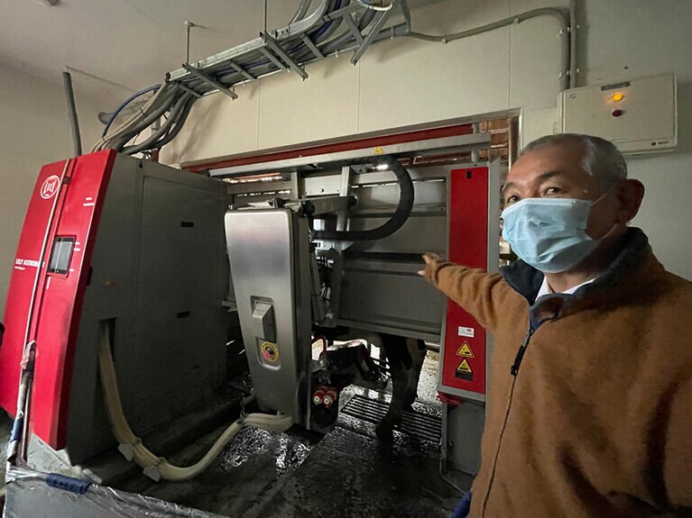 搾乳ロボットの説明をしてくださるのは、浜中町農業協同組合の高橋さん。右手の下に牛の黒い足が見える。左下のホースの中を白い生乳が流れていく。