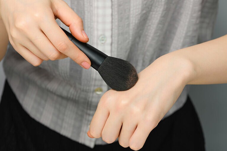 手の甲でパウダーをブラシの中に入れ込む。