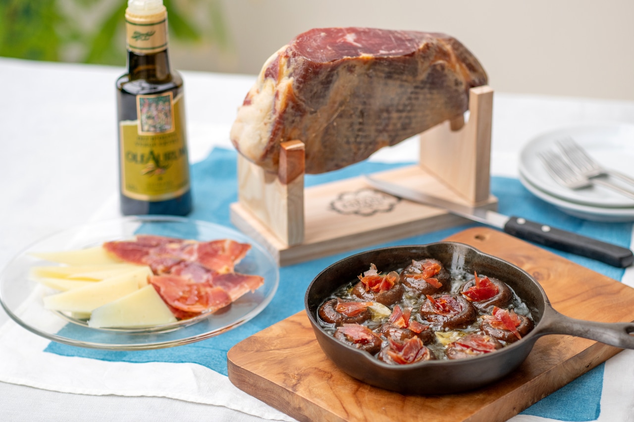 ホームパーティーなど人が集まる時に活躍するのは、リッチな食材が届くFコース“ファ―ストクラス”。原木生ハム風のブロックの生ハムにスタンド、専用ナイフが付き、チーズ（ケソ・マンチェゴ）とEVオリーブオイルをセット。切りたて生ハムのアヒージョは絶品。