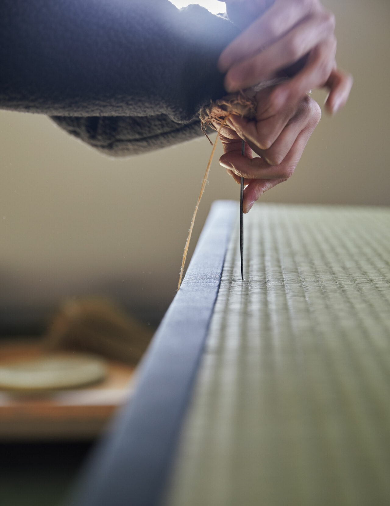 明るく陽が差し込む「横山畳工房」で。鉄板の入った畳職人用の道具「手当」を当て、もう一方の手を添えてぐっと畳針を刺す横山氏。空気に緊張が満ちる。