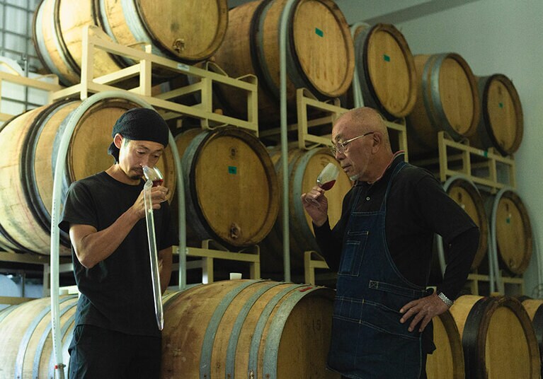 「テール ド シエル」代表の池田岳雄さん(右)と娘婿でもある栽培・醸造責任者の桒原さん。樽に眠るのは、2023年初めにリリース予定のメルロー。野生酵母で醸す自然の風味を大切にするため、過剰な樽香がつかぬよう、フランスから古い樽を輸入し使用。