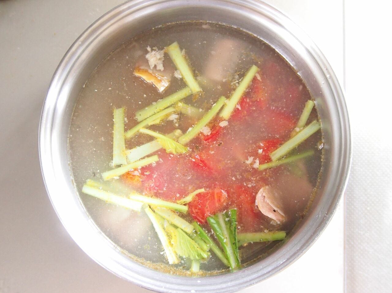 鍋に水、鯖の水煮缶、トマト、小松菜の茎の部分を入れて加熱する。