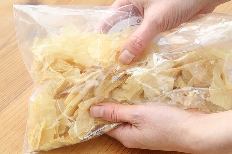 湯葉はジッパー付きの袋などに入れて、手で細かく砕く。綿棒で叩くようにしても良い。フレークタイプの乾燥湯葉。砕く前。