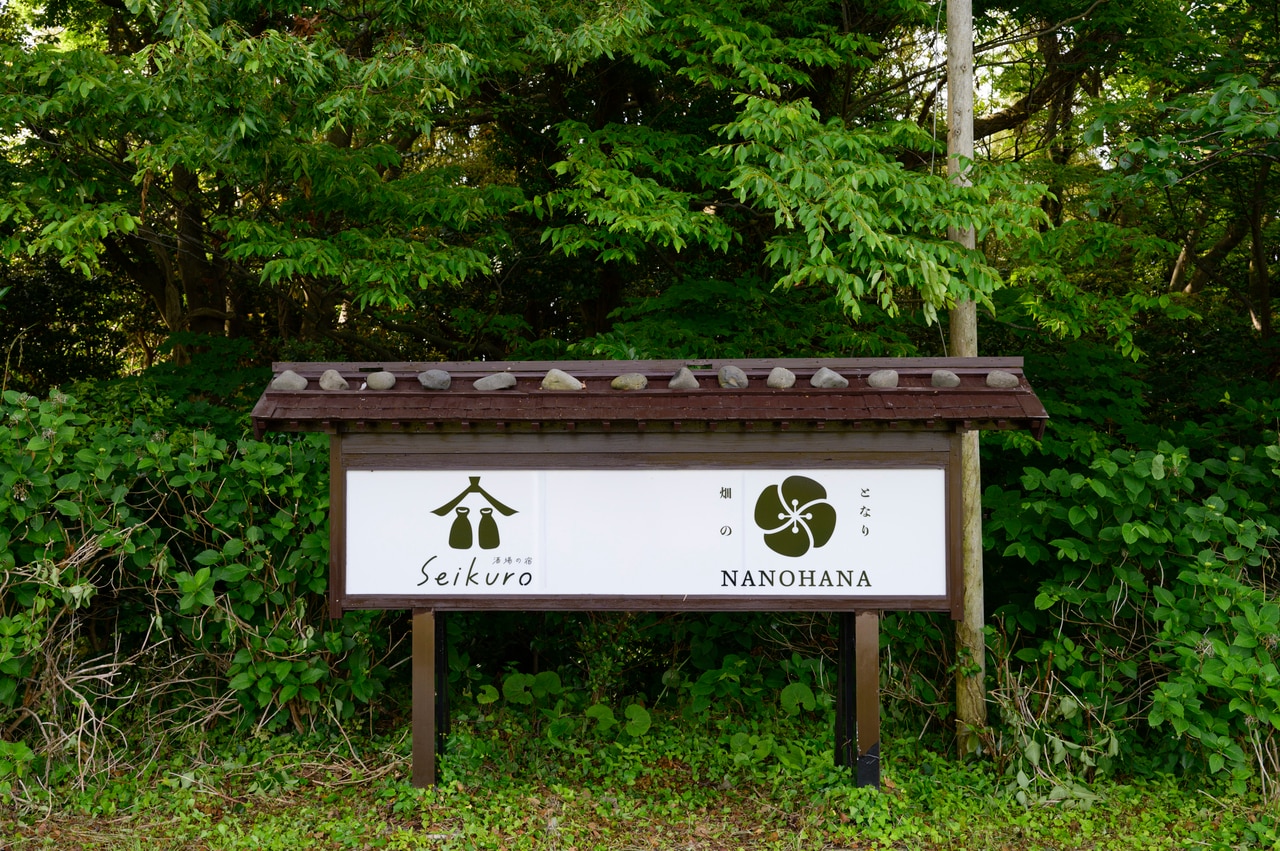 宿と「菜の花」の看板。「酒場の宿」をコンセプトに、畑と海が見える部屋と地の食材、地酒を揃えた酒場を提供。