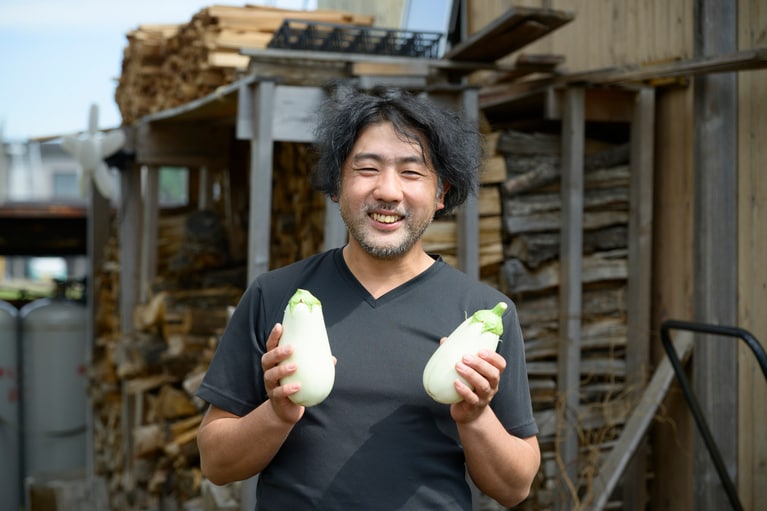 白いナスを手に笑顔の、りんごあめなすを育てる「佐藤大農園」の佐藤さん。