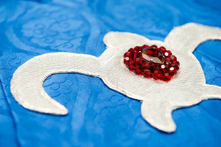 胸にあしらわれたナウシカを象徴するマークを近くでよく見るとストライプ状に銀糸で細かな刺繍が施されている。