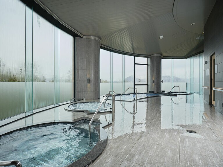 大きな窓から朝日や夕日の美しい自然光が大浴場を照らす大浴場。露天風呂やサウナ、トリートメントスパもある。