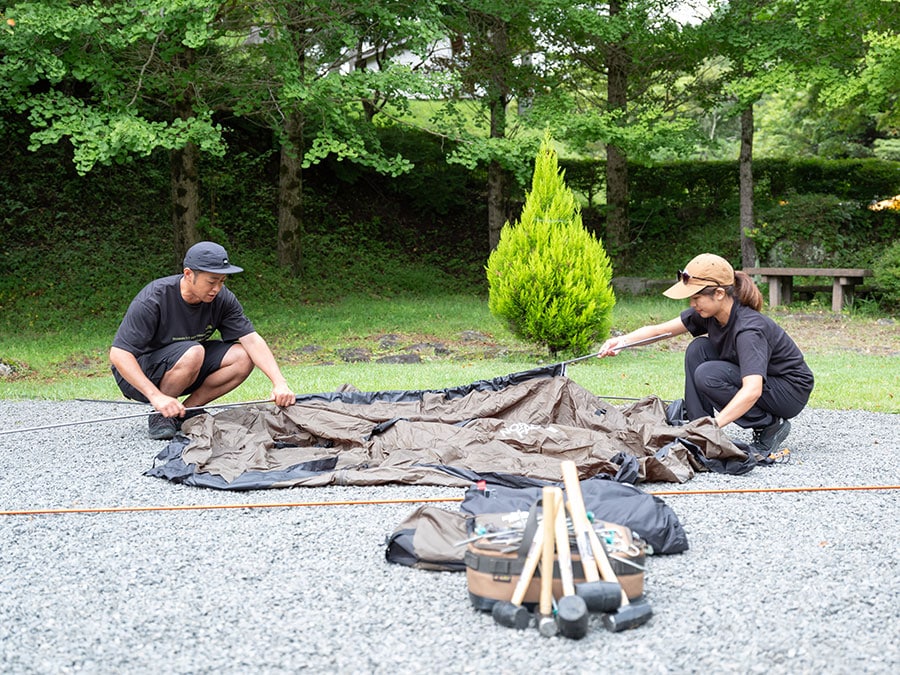 ザ・ノース・フェイスでキャンプギア開発を担当する野中研二さん（左）と大皿知可子さん（右）。設営するのは、大人4人が就寝でき、季節を問わず使える万能テント「Lander 4」（77,000円）。組み立てる前に、テントを広げておくと作業がしやすくてGood。