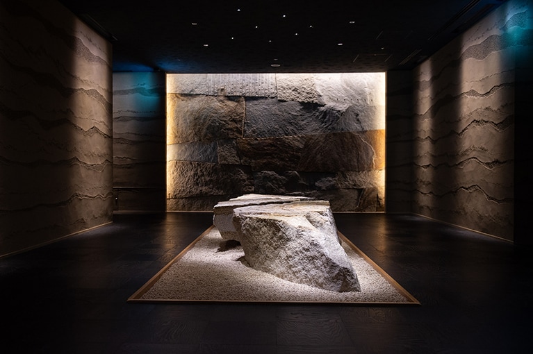 地層をイメージした左官仕上げの壁と大きな岩に迎えられるダイニングは隠れ家のよう。