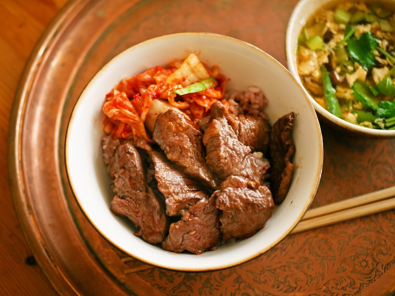 ある日の「たんぱく質とりたい日の丼」、手ごろな牛肉を焼いて、どっさりのせる。右は三つ葉としいたけと溶き卵の中華風スープ。三つ葉は2人前で1束入れてもするっと食べられる。