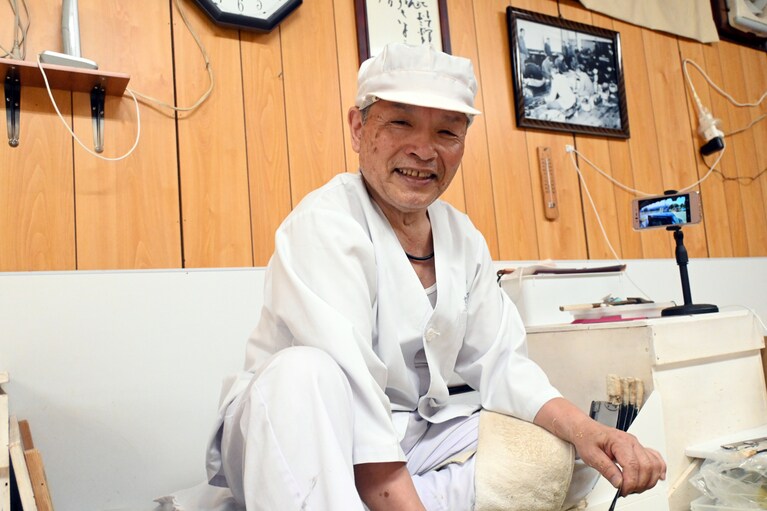 高橋衛さん。背後にはお父さんやおじさん、先輩職人の写ったモノクロームの写真が。