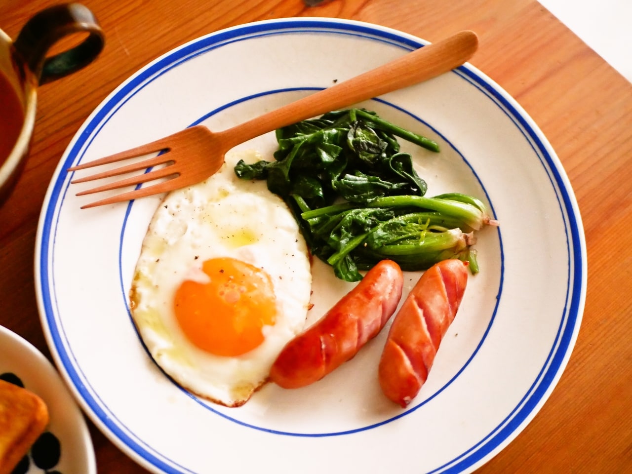 ゆでておいたほうれん草、ある日の朝食に。バターソテーにしつつ、同じフライパンで卵とウィンナーも焼く。