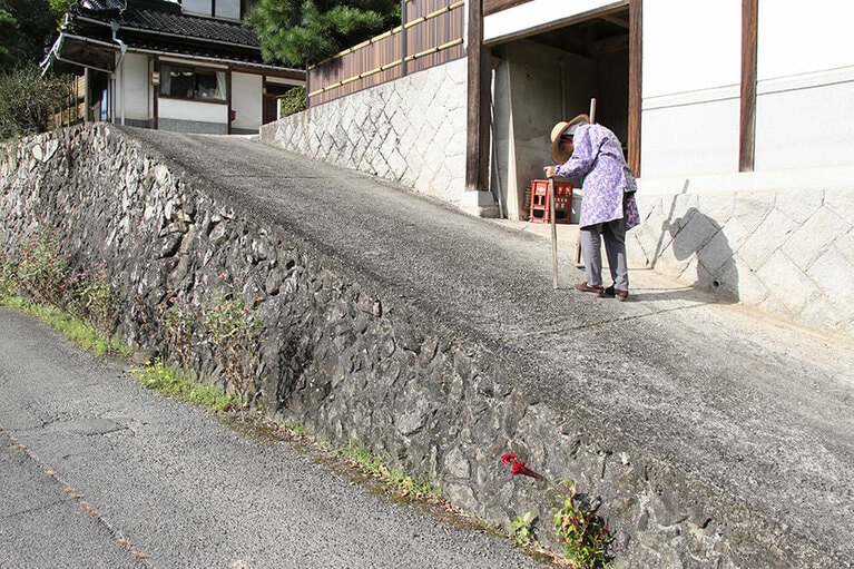 自宅の前の坂を杖をついてバックバックで下りる哲代おばあちゃん