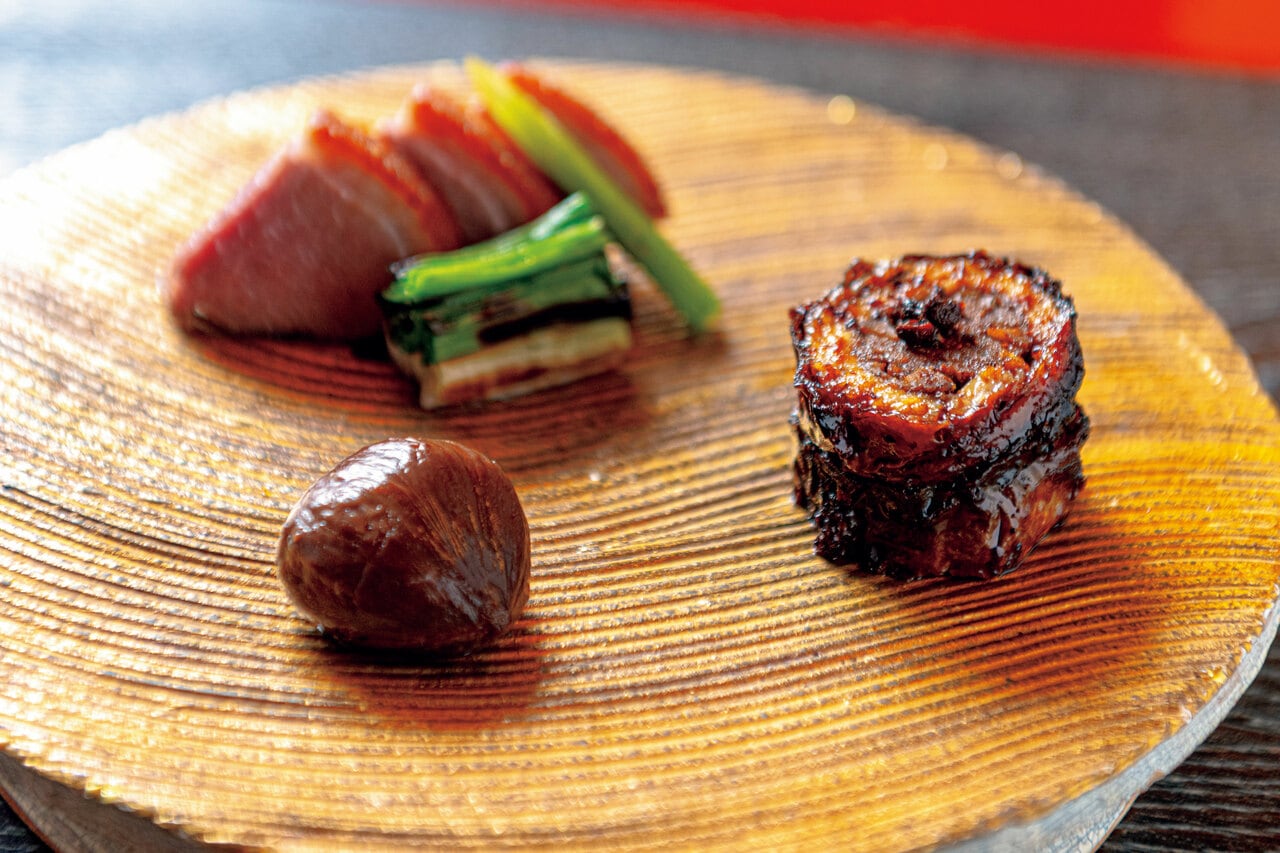 冬の献立「真味自在」の主菜は、熊挽肉を巻いた鰻の丹波産赤ワインソース風味と、パリッと焼き上げた鴨肉の盛り合わせ。鴨は皮目に細かな包丁目を入れてパウダー状にした八ッ橋をすり込んでいるため、ほのかな甘い香りが楽しめる。付け合わせは栗の甘酢漬け。