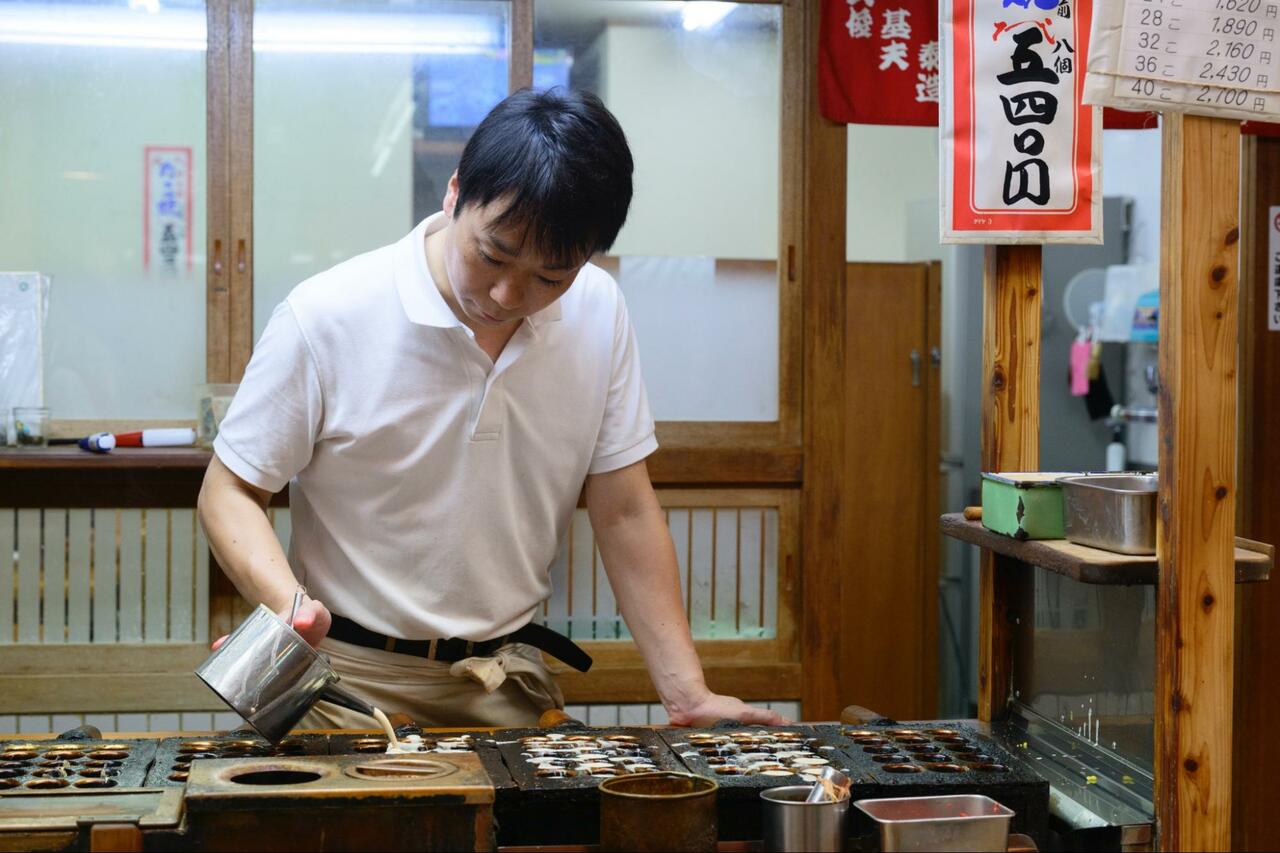 店頭でたこ焼きを焼く店主。お店は「天五中崎通商店街」の一角にある。