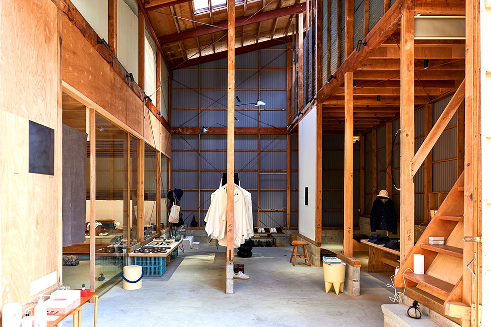 自然豊かな郊外の住宅地に立つ材木倉庫をリノベーション。奥には履物店「履物関づか」が。