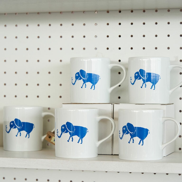 「青い象」が描かれたマグカッやTシャツ、クッキーといったおみやげグッズも販売。象の鼻カフェのアイコン「青い象」はミナ ペルホネンのデザイナー、皆川明氏によるもの。