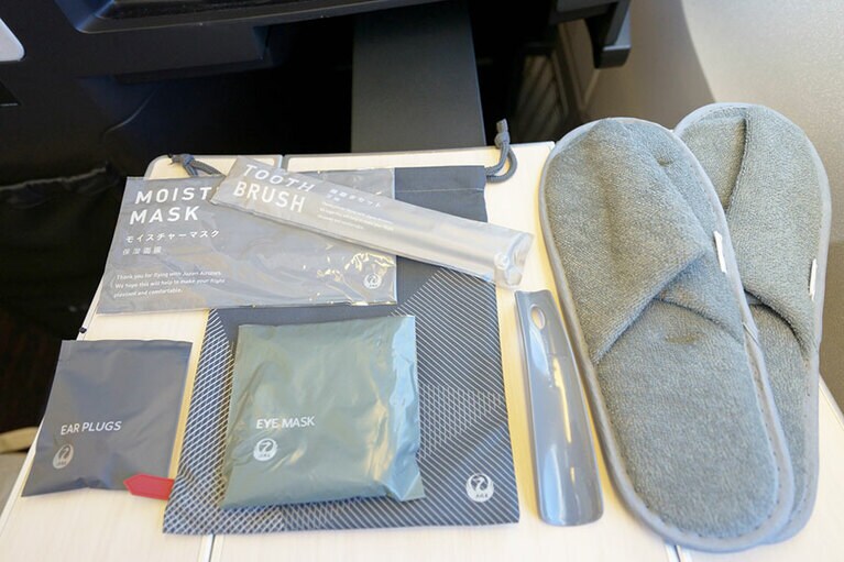 ロゴ入りポーチに入ったアメニティはアイマスク、モイスチャーマスク、歯ブラシ、イアプラグ。ふかふかのスリッパには靴ベラもついている。