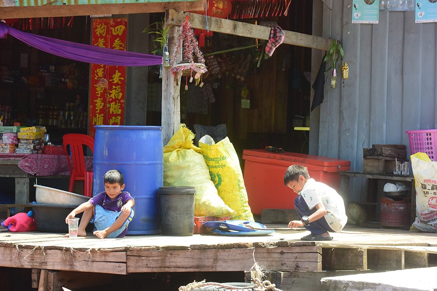 野菜や雑貨、洋服を売る、水上のよろず屋の前で遊ぶ子供たち。